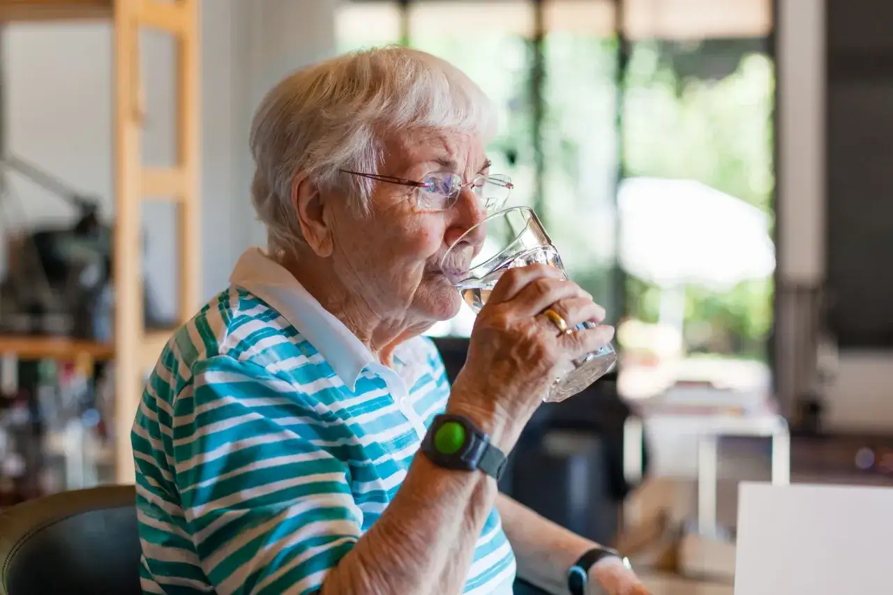 Une femme &acirc;g&eacute;e boit un verre d'eau, assurant son hydratation optimale.