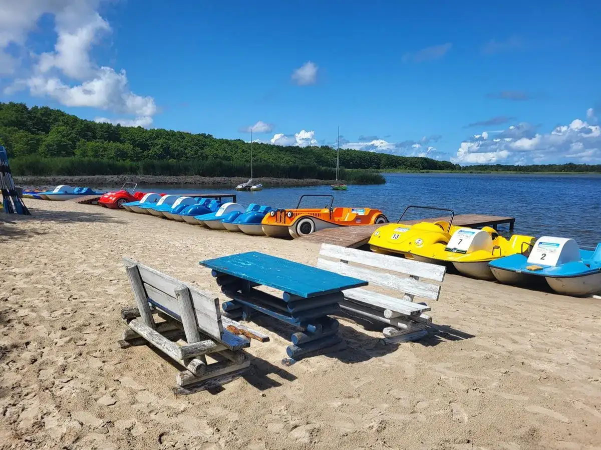 Słoneczny dzień nad jeziorem Sarbsko plaża. Rząd kolorowych rowerk&oacute;w wodnych czeka na plaży, gotowych do wodnych przyg&oacute;d.