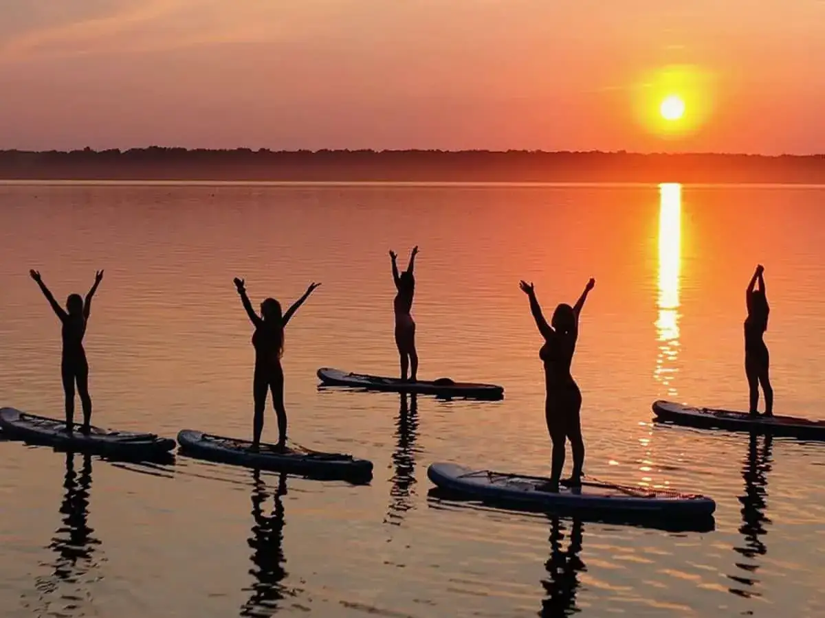 Silhouetten von Frauen, die bei Sonnenuntergang auf SUP-Boards Yoga machen.