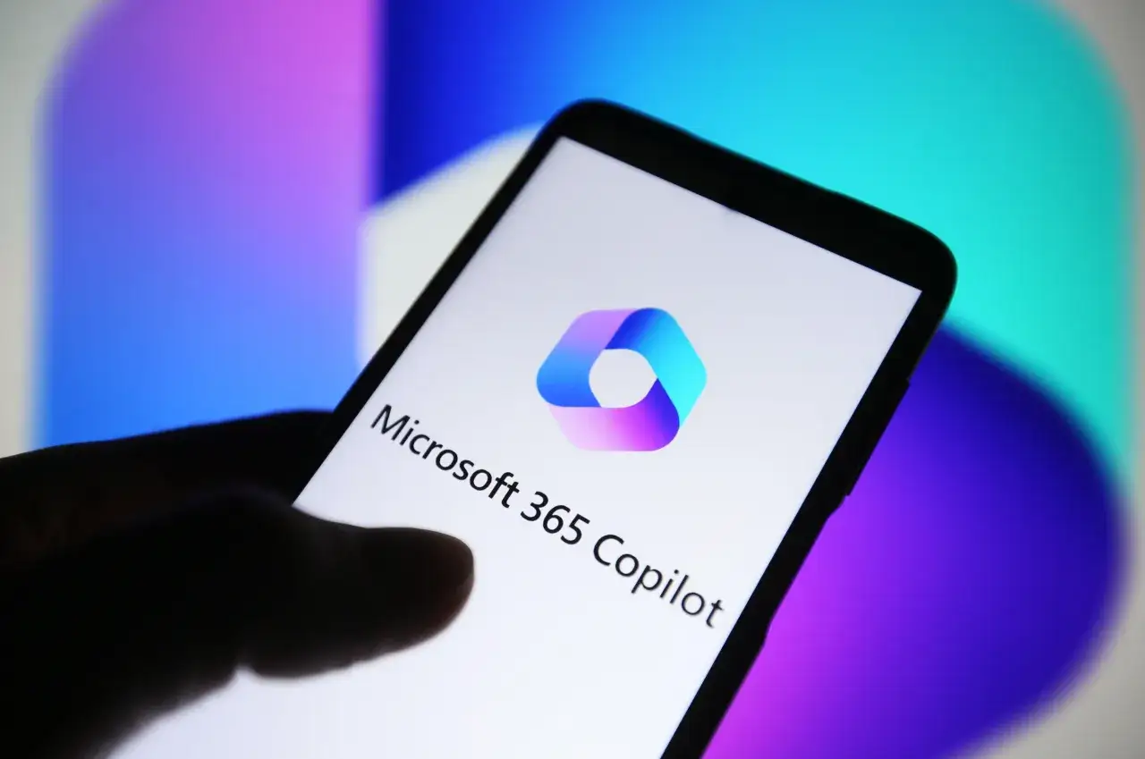 Dłoń trzyma smartfon z logo Microsoft 365 Copilot. Tło to gradient fioletu i błękitu.