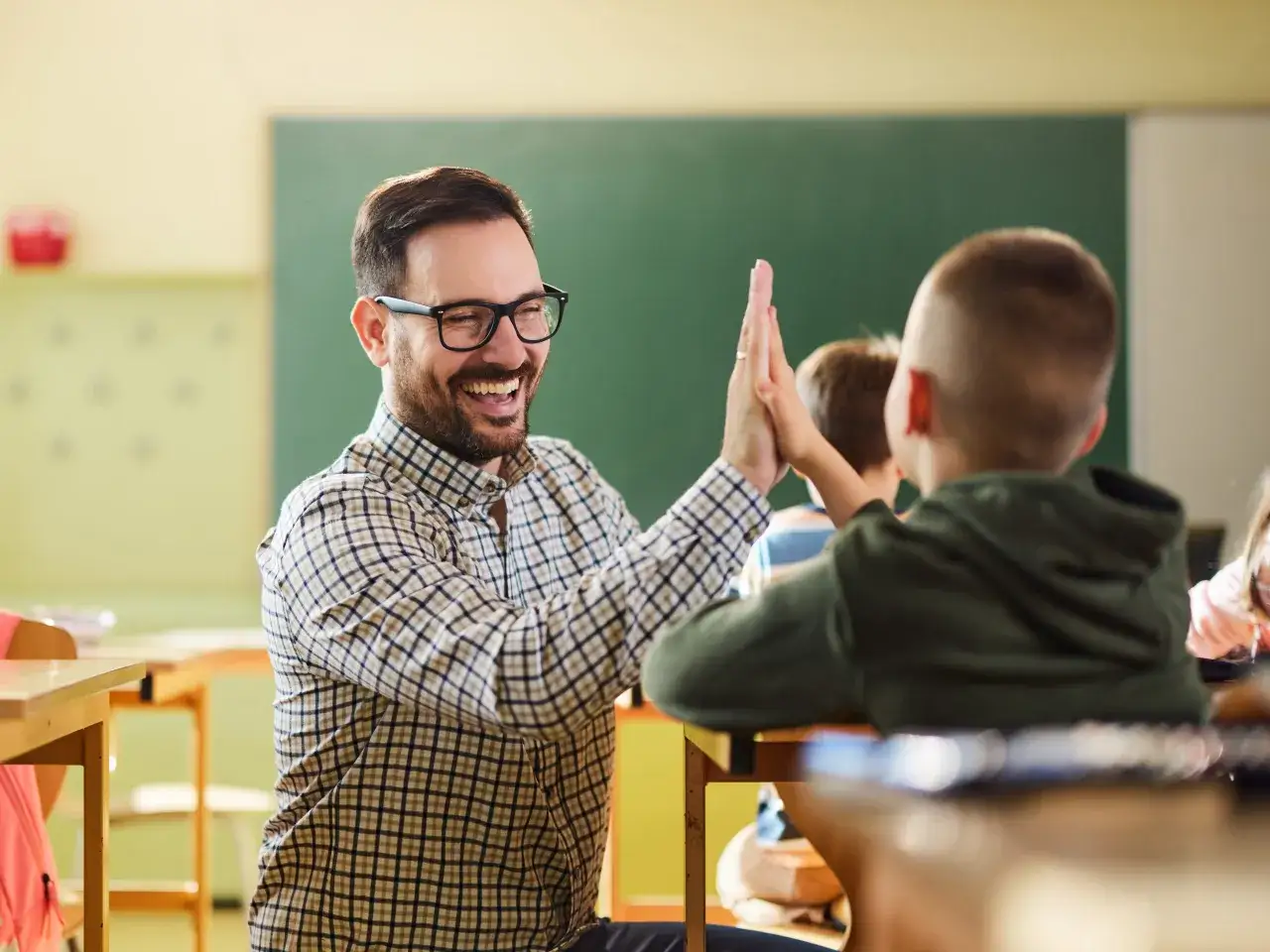 Lehrer und Schüler geben sich in der Schule einen High Five. Ein Beispiel für gewaltfreie Kommunikation im Klassenzimmer.