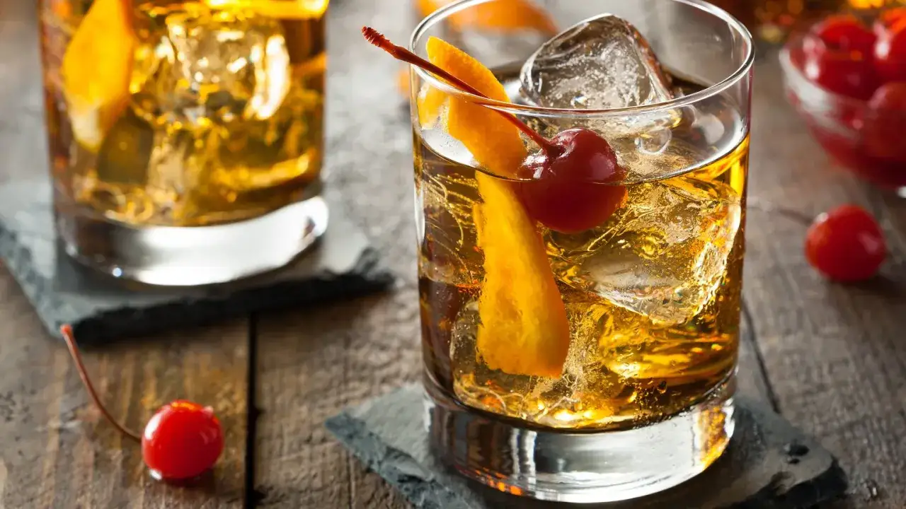 Klasyczny Old Fashioned przepis: bursztynowy alkohol, lód, skórka pomarańczy i wisienka. Idealny na wieczór.
