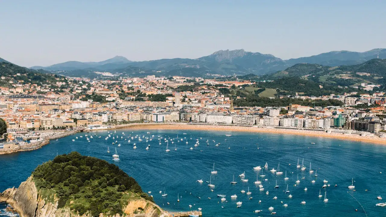 A panoramic view of San Sebastián's bay, with boats dotting the blue water and a crowded beach. This scene inspires thoughts of perfect day trips from San Sebastian.