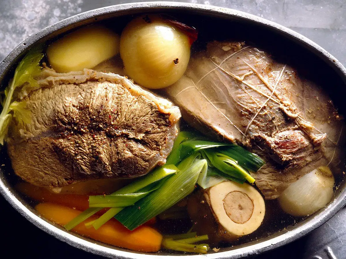 Un plat mijoté, parfait pour une recette pot au feu : morceaux de bœuf, légumes (carottes, poireaux, oignons, pommes de terre) dans un bouillon.