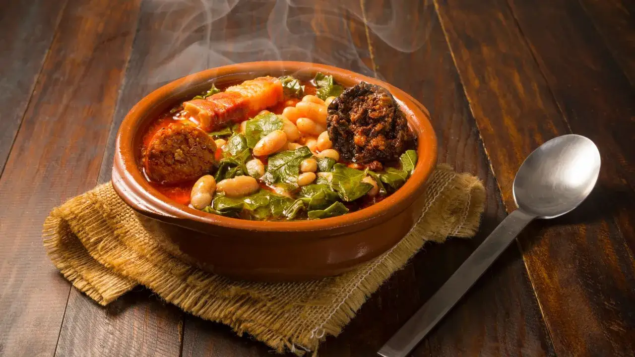 Un humeante pote asturiano, con fabes, berzas, chorizo y tocino, servido en cazuela de barro sobre arpillera.