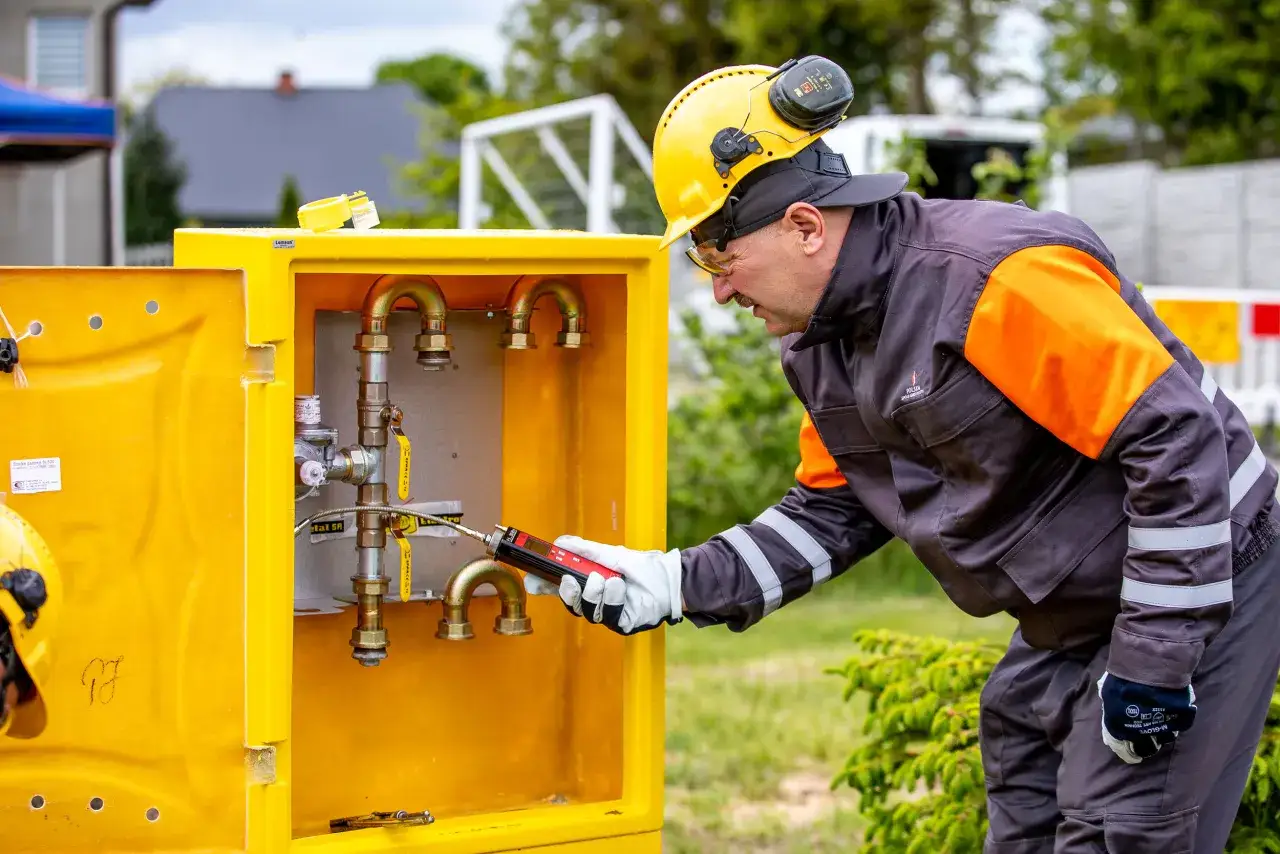 Pracownik w żółtym kasku sprawdza instalację gazową w żółtej szafce. Sprawdź pogotowie gazowe cennik usług.