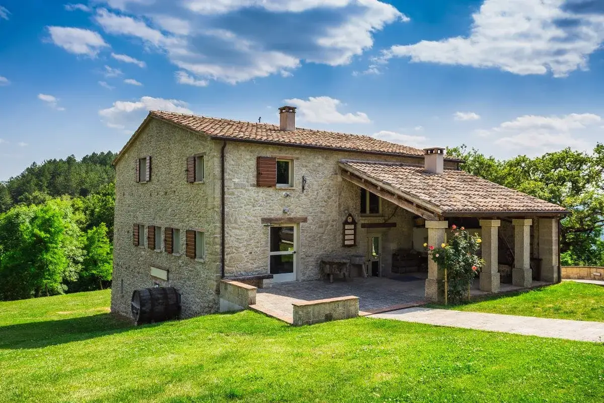 Belle ferme en pierre, résultat d'une rénovation réussie, nichée dans un paysage verdoyant sous un ciel bleu.