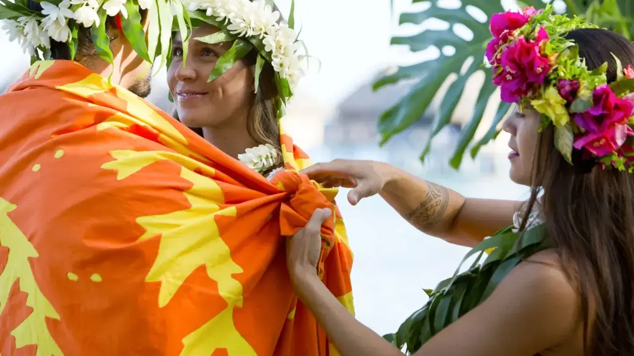 Coppia in un matrimonio misto, adornata con ghirlande di fiori e un drappo colorato. Un momento di unione e celebrazione.
