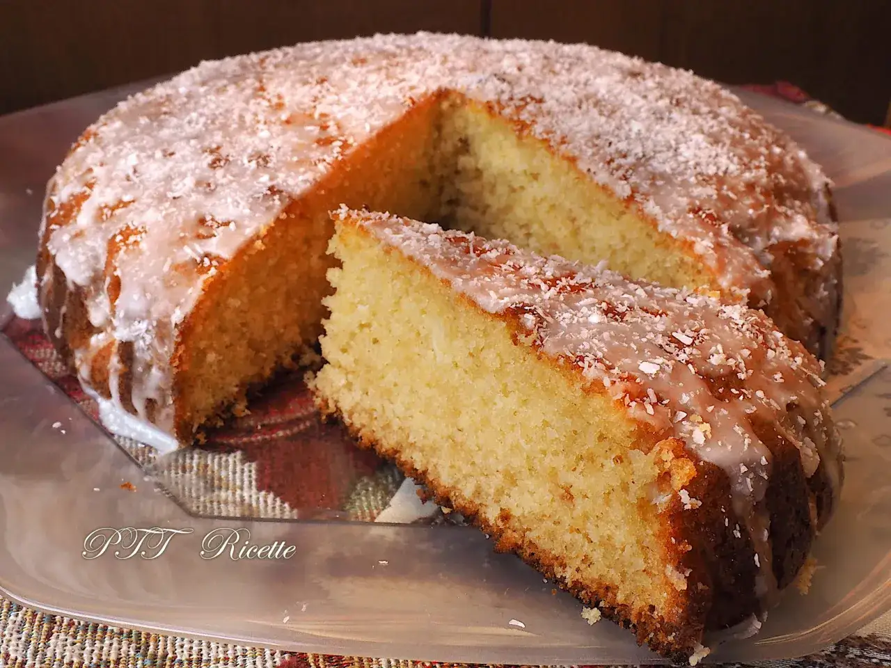 Deliziosa torta al cocco, soffice e profumata, con glassa bianca e scaglie di cocco. Una fetta è già stata servita.