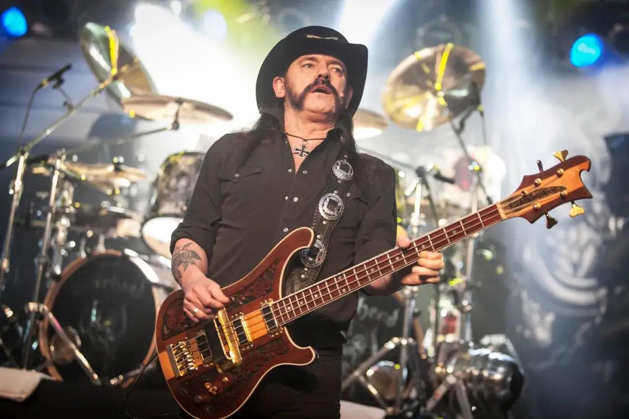 Lemmy Kilmister, ikona rocka, gra na basie na scenie. W tle widać perkusję jego zespołu.