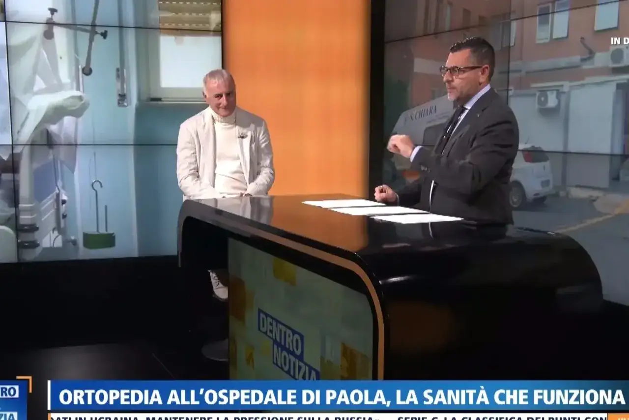 Due uomini discutono in studio. Uno parla di quanto prende un primario, mentre sullo schermo si vede un ospedale.