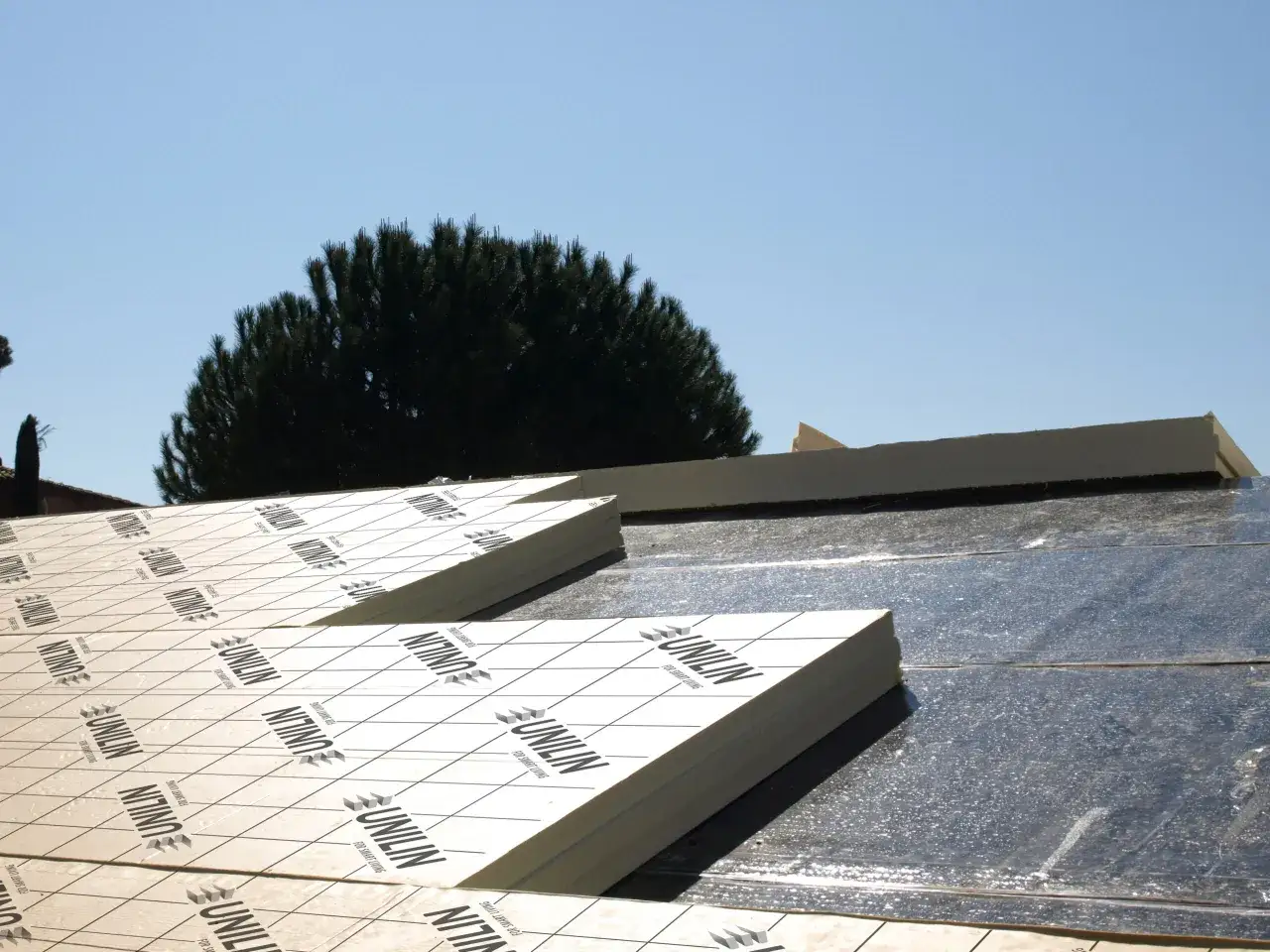 Panneaux de polyur&eacute;thane pour isolation toiture par l'ext&eacute;rieur. Un chantier en cours sous un ciel bleu.