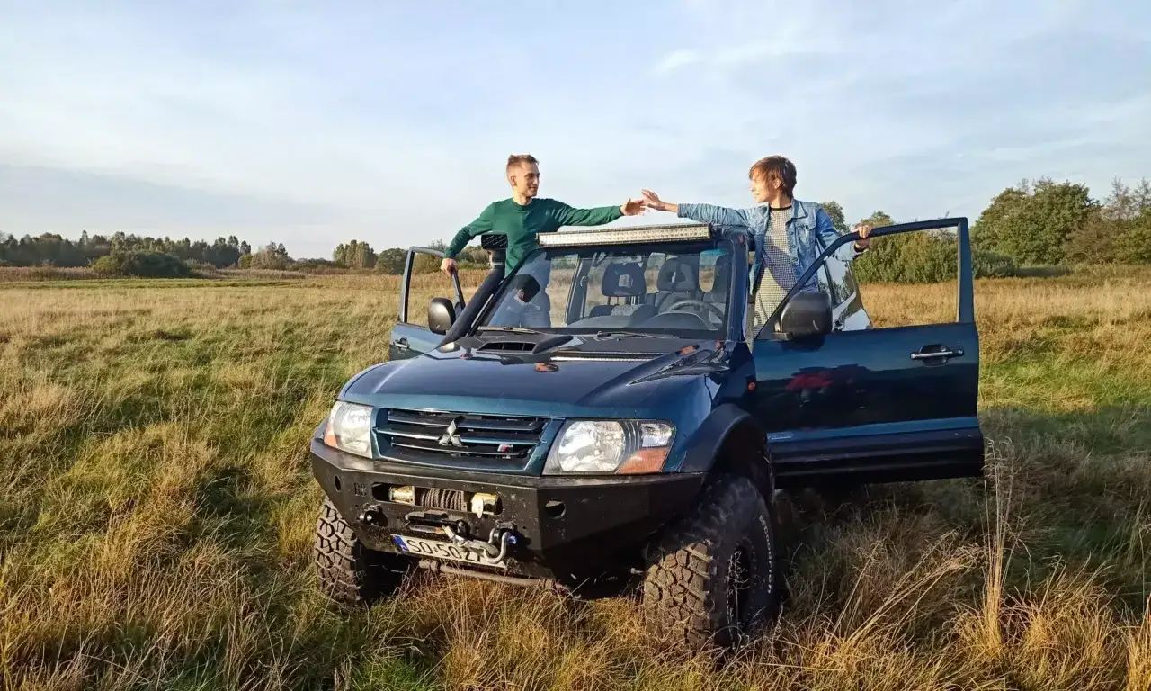 Dwóch przyjaciół przy terenowym Mitsubishi Shogun w słoneczny dzień na łące.