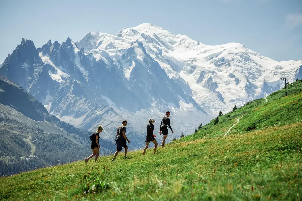 Quatre randonneurs gravissent une pente verdoyante, le Mont-Blanc enneigé en toile de fond. Une belle randonnée à Chamonix.