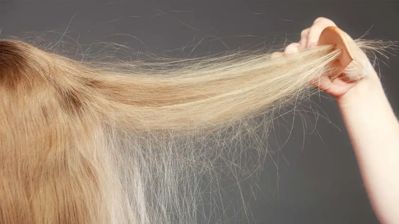 En hand håller en träkam genom blont hår som visar tydliga kluvna toppar.