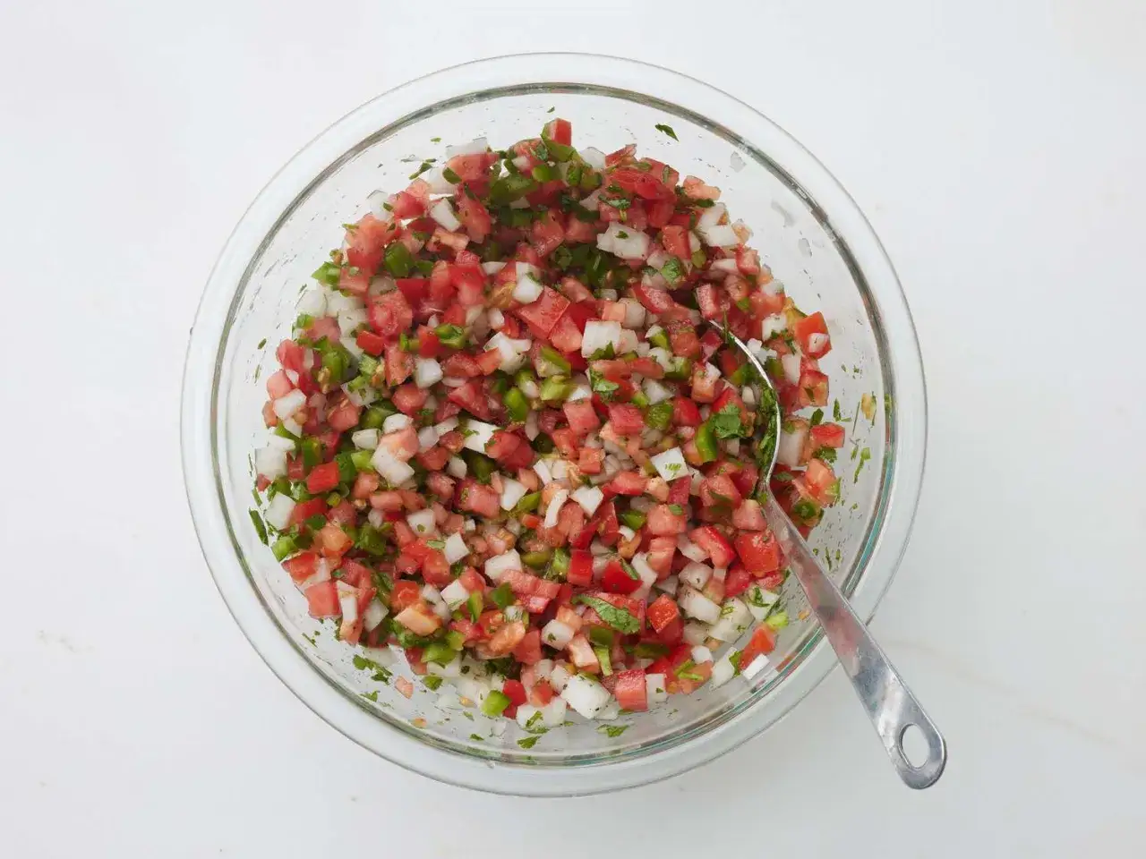 En skål med färsk pico de gallo, en blandning av hackade tomater, lök, jalapeño och koriander, med en sked redo att servera.