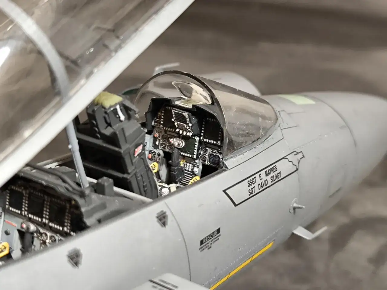 Detailgetreues Cockpit eines Kampfjets mit detaillierter Instrumententafel und Sitz. Eine kleine Pilotenpuppe sitzt bereit für ihren Einsatz.
