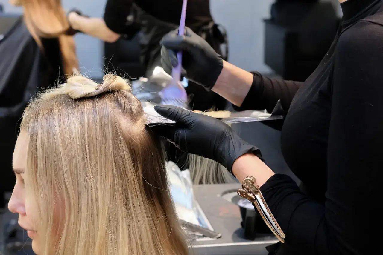 Frisör applicerar färg i en kunds ljusblonda hår.