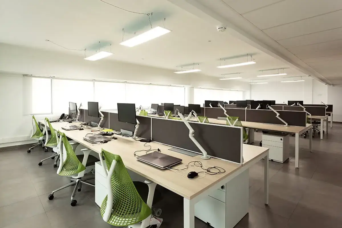 Bureau moderne et lumineux, prêt pour le **digital workplace**. Rangées de postes de travail avec écrans, chaises vertes vives et cloisons grises.