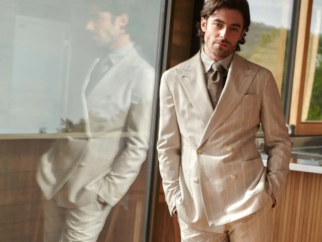 A man in a light-colored, double-breasted suit with subtle pinstripes, embodying the perennial suit meaning of timeless style.
