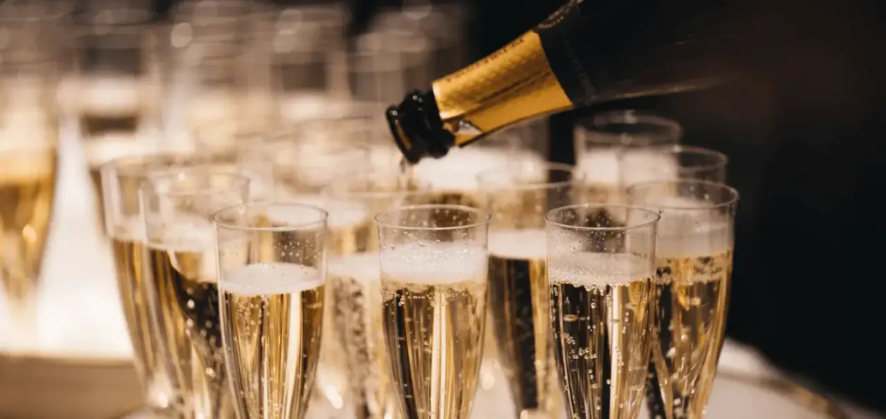 Une bouteille de champagne verse son contenu p&eacute;tillant dans une rang&eacute;e de fl&ucirc;tes. Difficile de dire combien de coupe dans une bouteille de champagne, mais la f&ecirc;te est lanc&eacute;e !