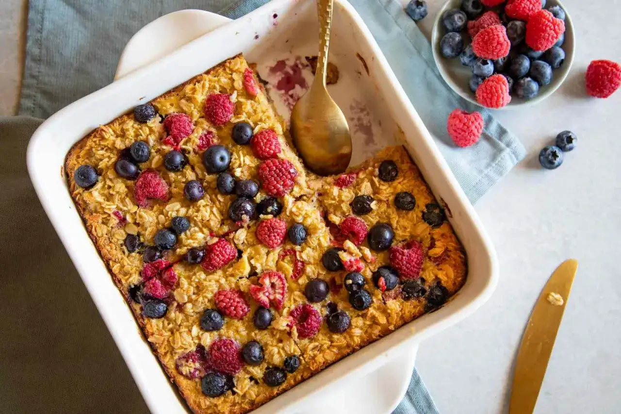 Leckeres baked oats rezept mit frischen Beeren in einer Auflaufform. Ein goldener Löffel wartet darauf, probiert zu werden.