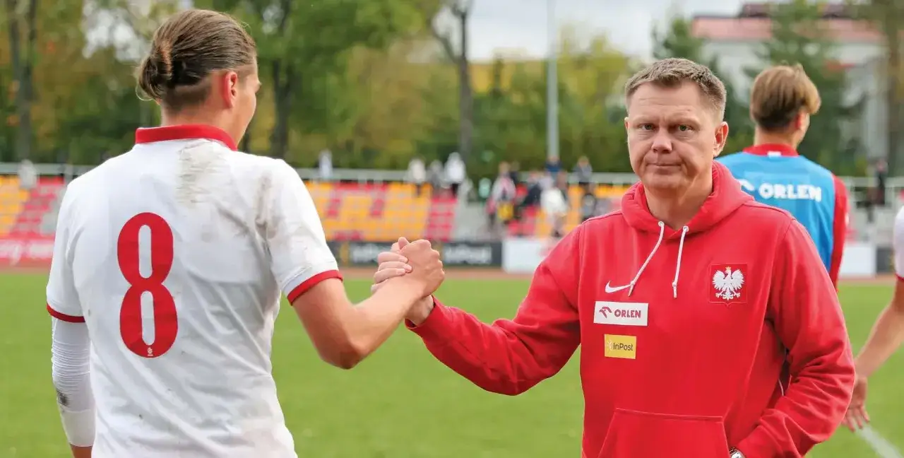 Trener piłkarski w czerwonej bluzie z orłem i zawodnik z numerem 8 na koszulce ściskają sobie dłonie. To inspiracja, jak zostać trenerem piłki nożnej dla dzieci.