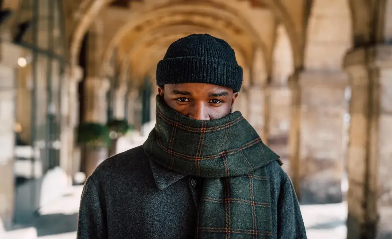 Uomo con berretto nero e sciarpa a quadri verde, un esempio di come indossare un berretto uomo con stile per proteggersi dal freddo.