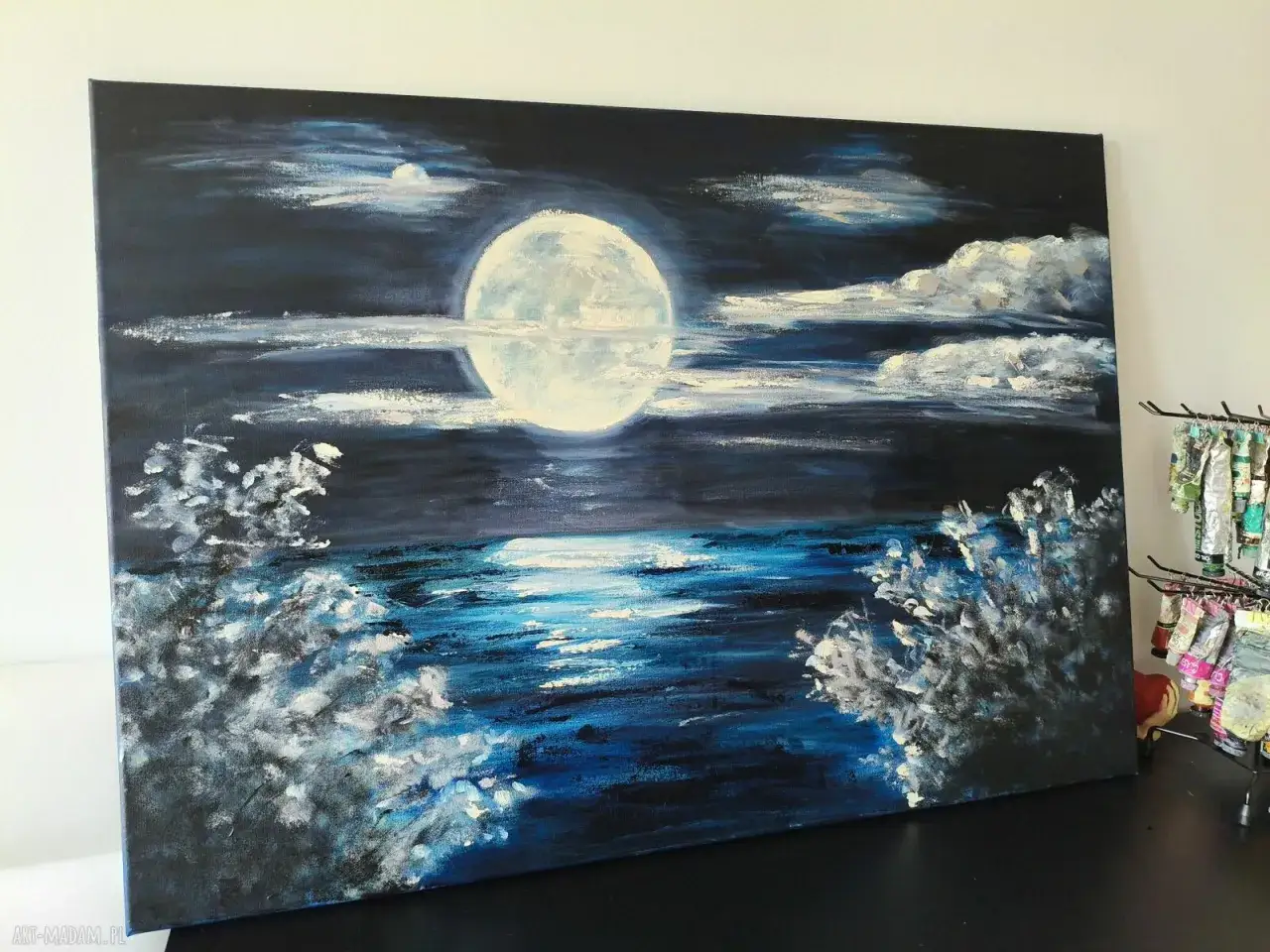 Nocny obraz miasta nad wodą, z wielką, jasną księżycem odbijającą się w falach.