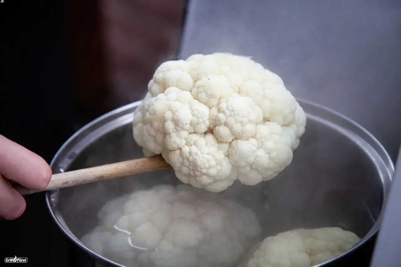 Blumenkohl wird mit einem Holzl&ouml;ffel aus kochendem Wasser gehoben, ein wichtiger Schritt beim Blumenkohl einfrieren.
