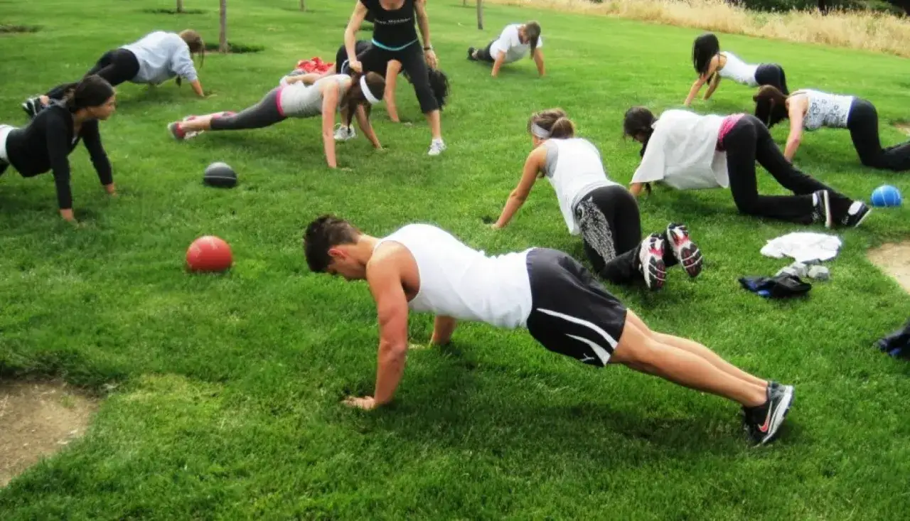 Un groupe de personnes participe à un boot camp sportif, effectuant des pompes sur l'herbe.