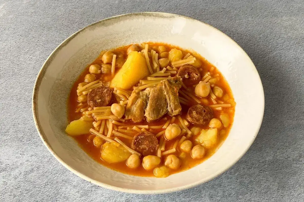 Un reconfortante rancho canario con garbanzos, fideos finos, patatas, chorizo y trozos de carne en un cuenco r&uacute;stico.