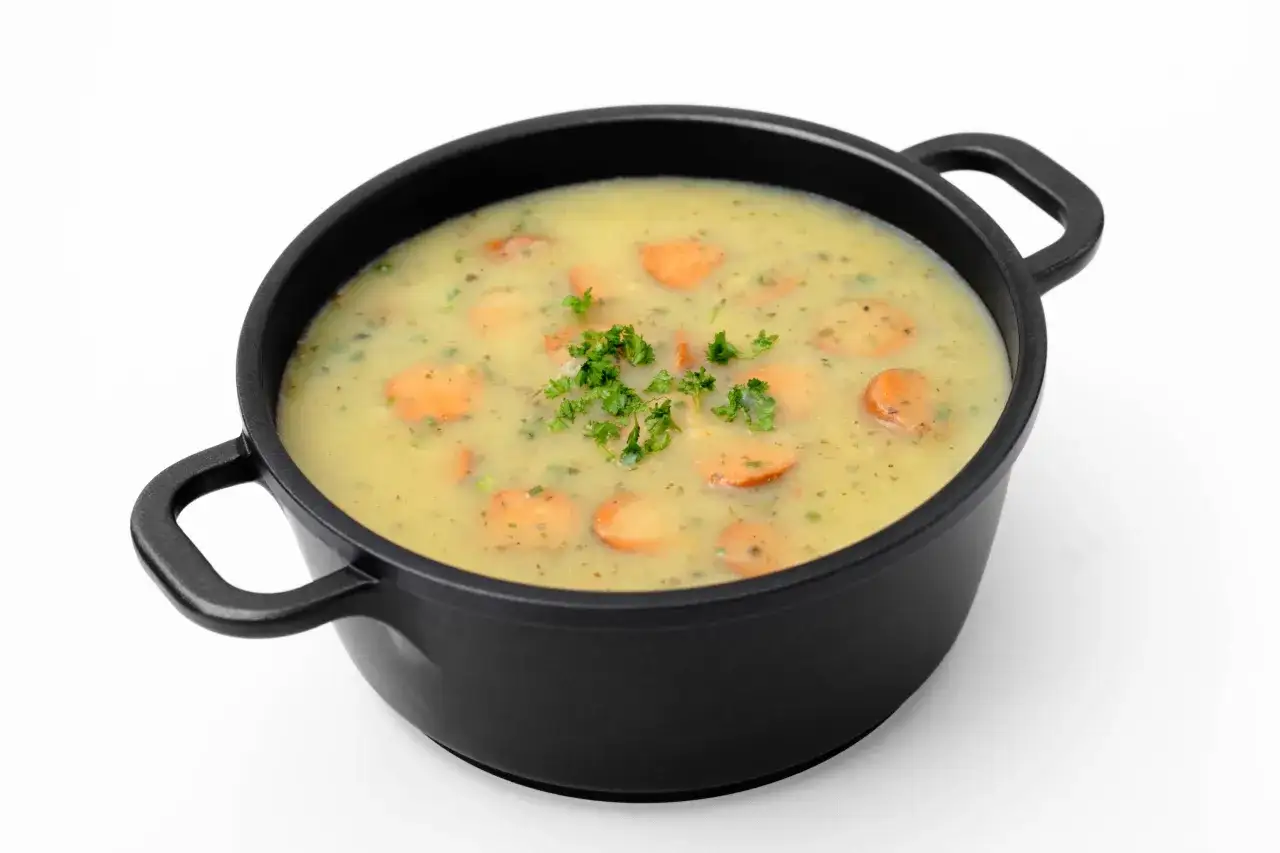 Eine cremige Gemüsesuppe mit Karottenscheiben und Petersilie in einem schwarzen Topf, wie aus Omas Rezepten für das Mittagessen.