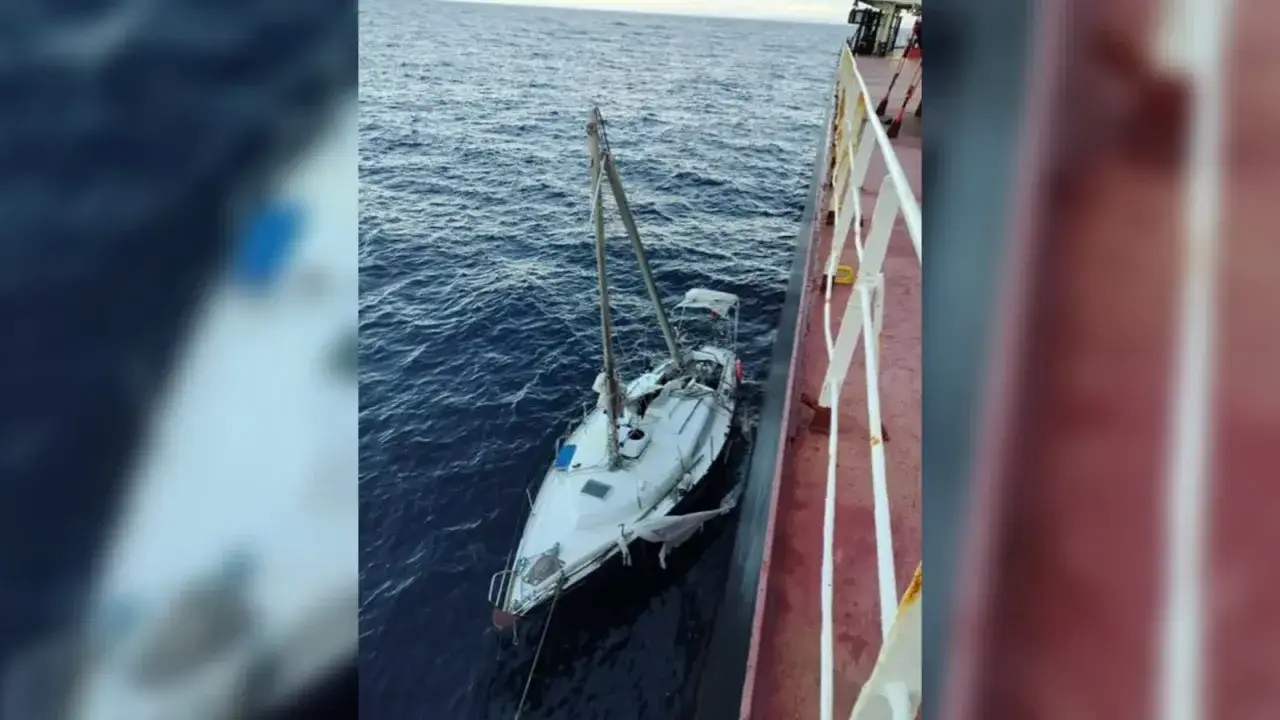 Un voilier blanc, endommagé, est à la dérive près d'un grand navire. L'accident de voilier semble avoir causé des dégâts importants à la voile.