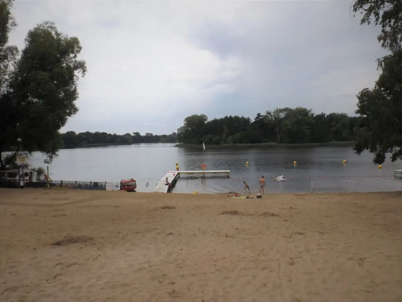 Plaża nad jeziorem koło Gniezna. Ludzie kąpią się i odpoczywają na piasku.