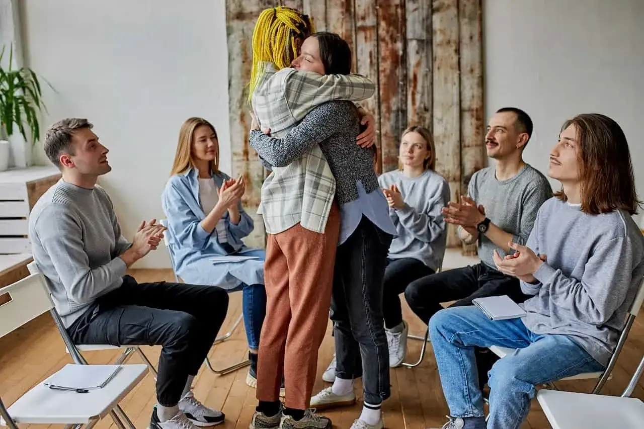Grupa wsparcia AA świętuje sukces. Dwie osoby przytulają się, reszta klaszcze.