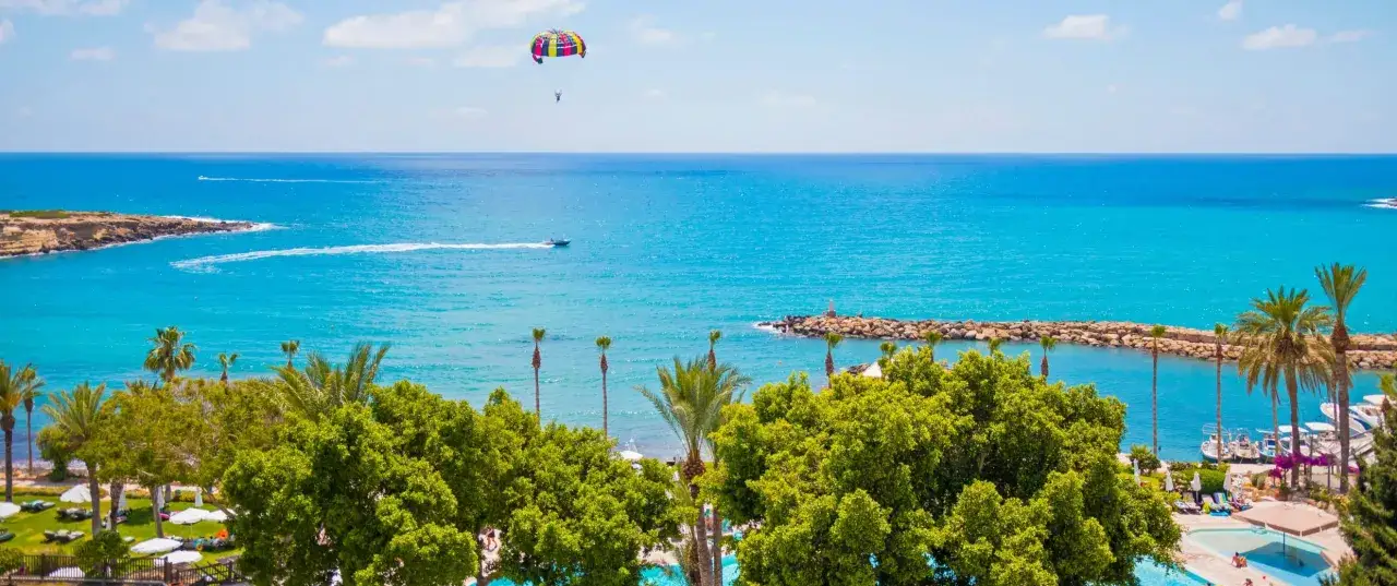 Rajska plaża na Cyprze, gdzie praca to przyjemność. Parasailing, łodzie i palmy nad turkusowym morzem.