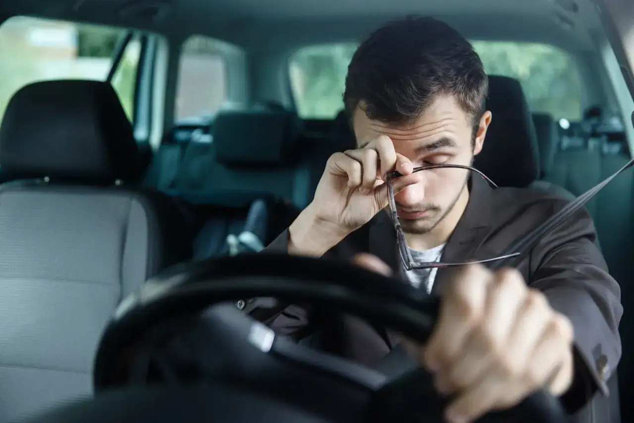 Hombre cansado se frota los ojos al conducir mucho tiempo sin descansar.