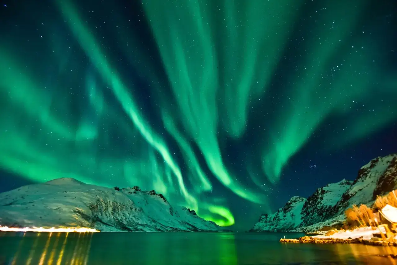 Spektakularna zorza polarna nad Tromsø, zielone pasma tańczą na nocnym niebie, odbijając się w spokojnej wodzie.