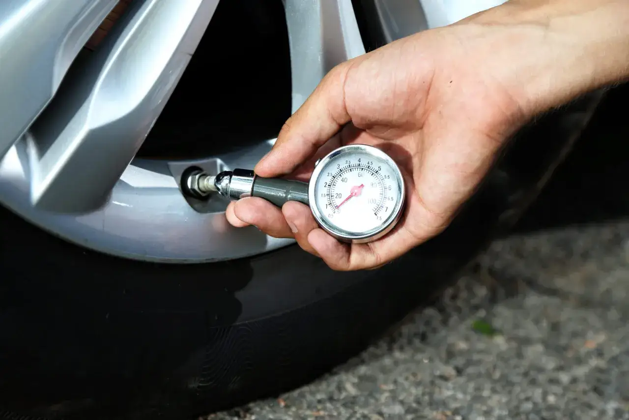 Mano usando un manómetro para comprobar como saber la presión de las ruedas del coche. El medidor muestra la presión en PSI y bares.