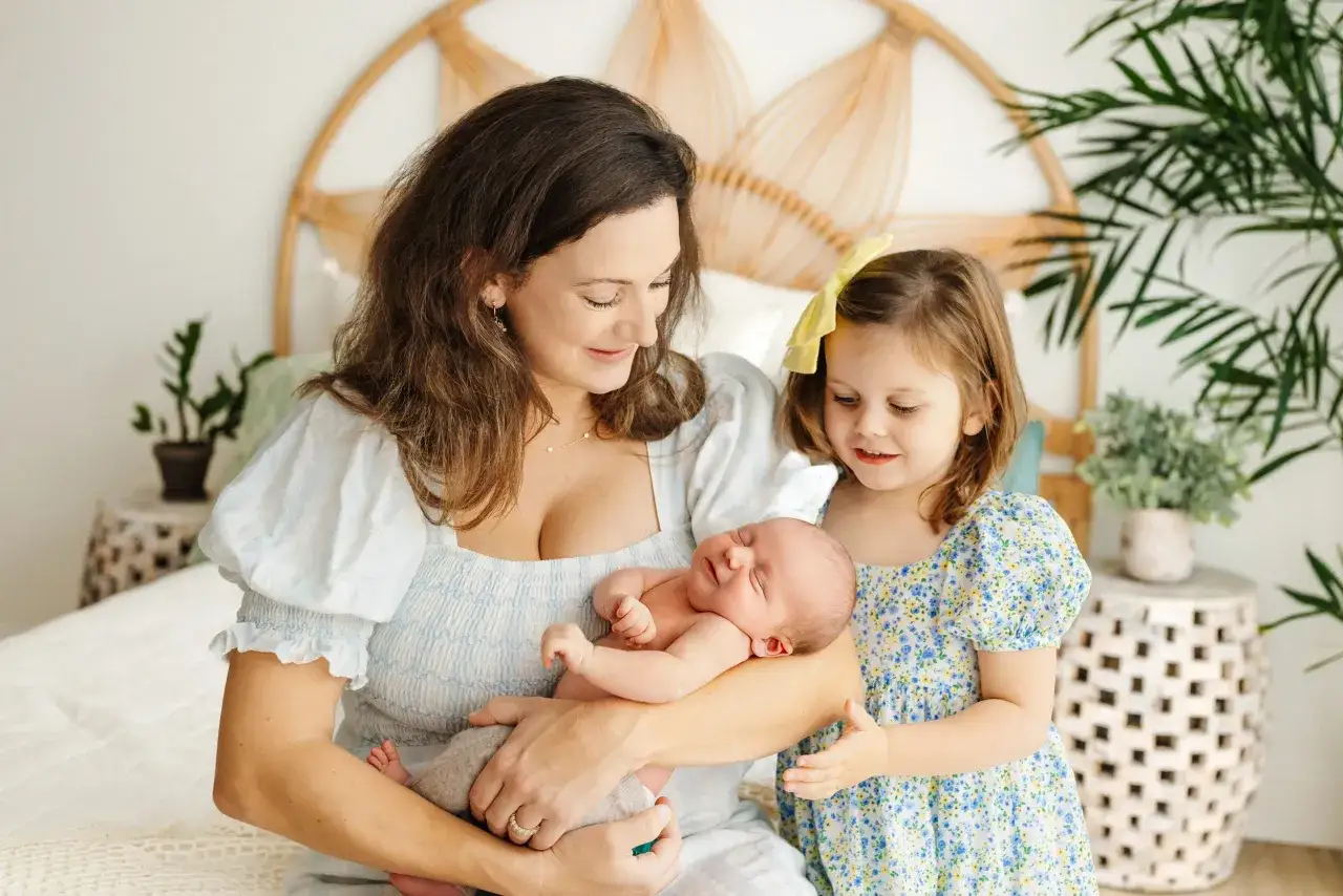 Mama tuli noworodka, a starsza siostra z zachwytem patrzy na braciszka. Piękna sesja noworodkowa z rodzeństwem.