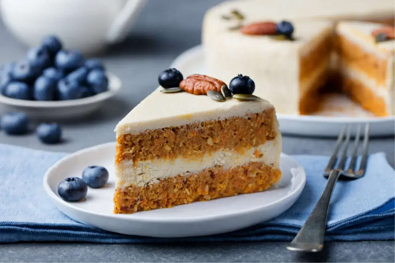 Ein Stück cremiger Karottenkuchen, dekoriert mit Blaubeeren und Nüssen. Diese veganen Kuchen sind ein Genuss!