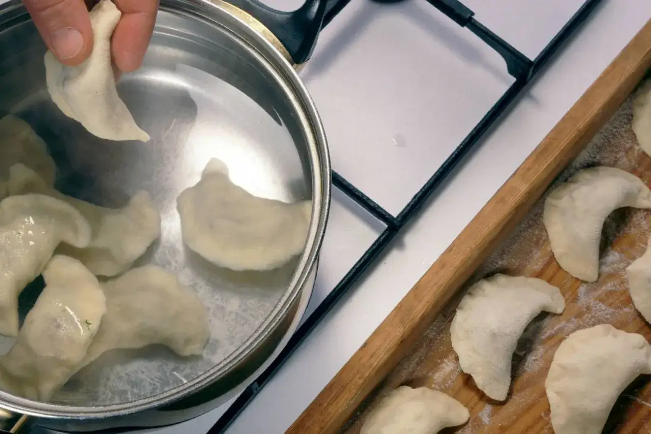 Gotowane pierogi w garnku z wodą i surowe na desce. Tak mrozic ugotowane pierogi, by cieszyć się nimi później.