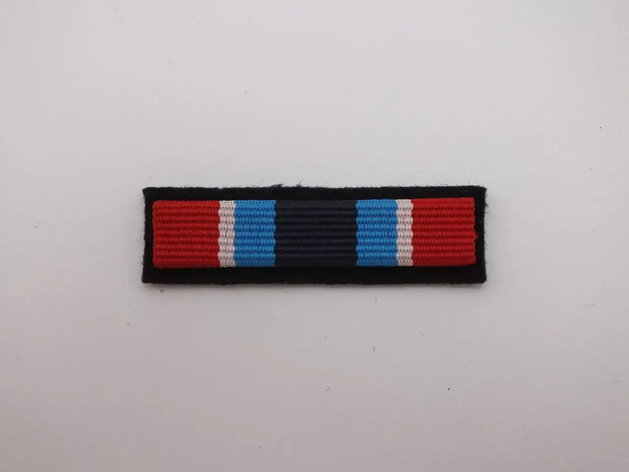 Wstążka z czerwonymi, białymi i niebieskimi pasami na czarnym tle, symbolizująca zasłużonego dla ochrony przeciwpożarowej.