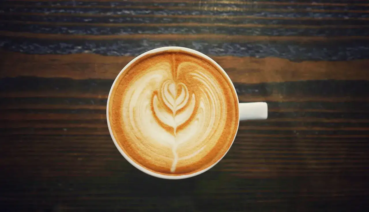 Kawa latte z pianką na drewnianym blacie. Czy kawa rozpuszczalna podnosi ciśnienie? Ta wygląda na świeżo zaparzoną.