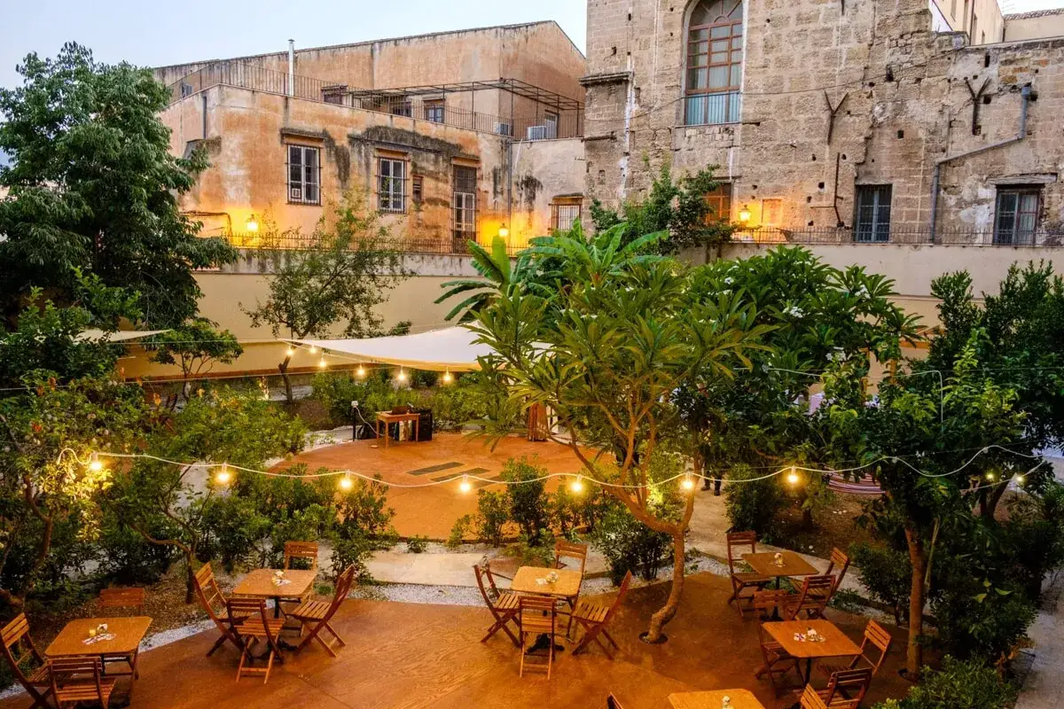 Giardino incantevole con tavoli apparecchiati, luci soffuse e vegetazione lussureggiante. Un'atmosfera magica, perfetta per scoprire i migliori ristoranti di Palermo.