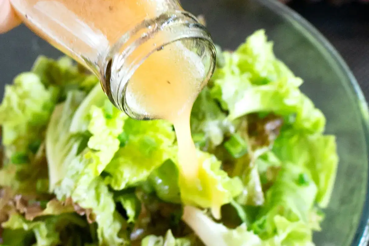 Se vierte una salsa para ensaladas de color naranja claro sobre una ensalada verde fresca en un bol de cristal.