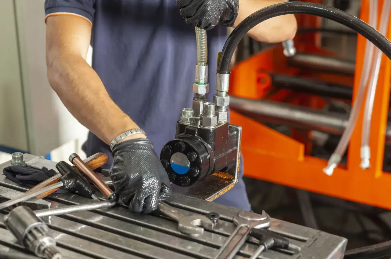 Mechanik w Grójcu montuje elementy hydrauliki siłowej. Na stole narzędzia i pompa.