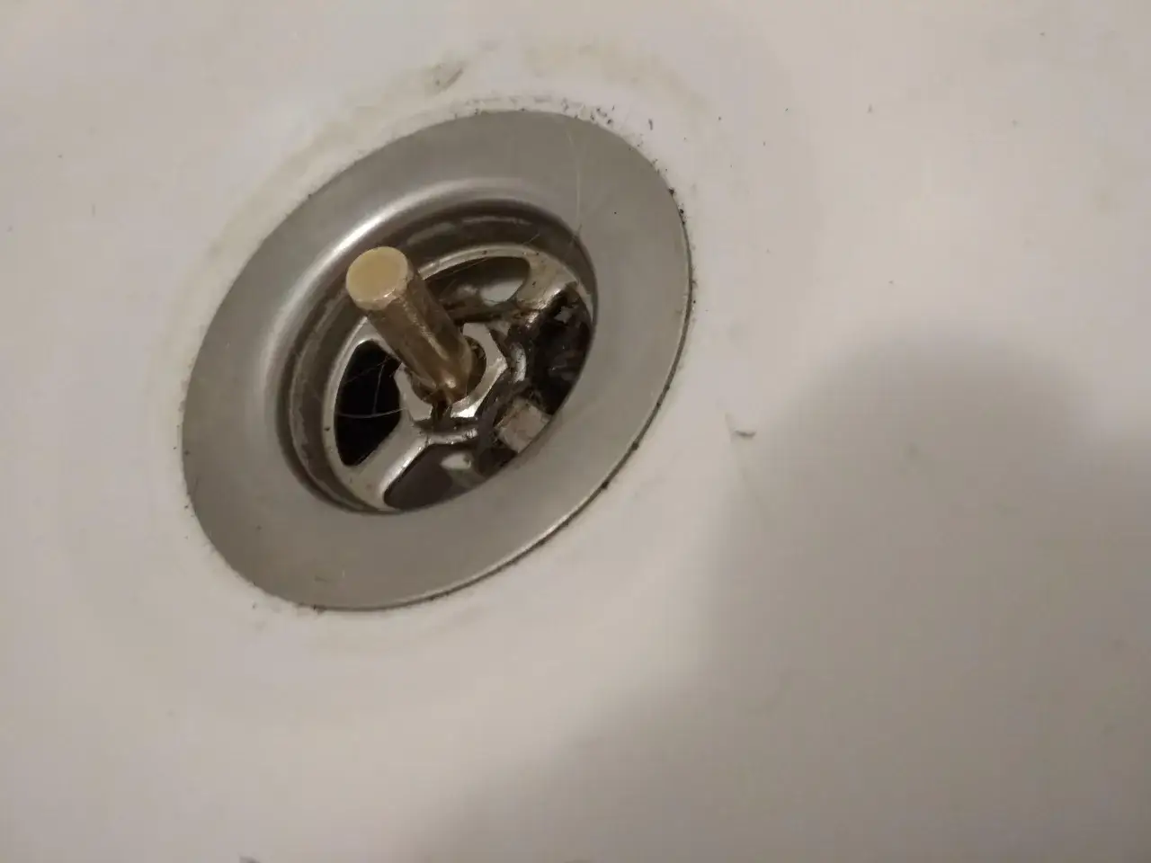 Korek do wanny z pokrętłem, widoczny mechanizm do naprawy. Widać włosy i brud wokół odpływu.