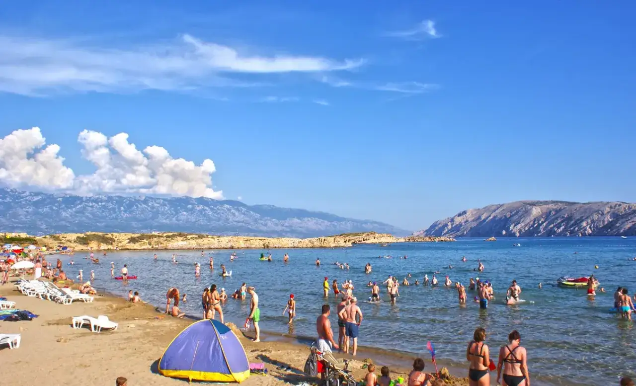 Wyspa Rab: plaża pełna ludzi, słońce, morze i góry w tle. Atrakcje dla każdego, od kąpieli po relaks na piasku.